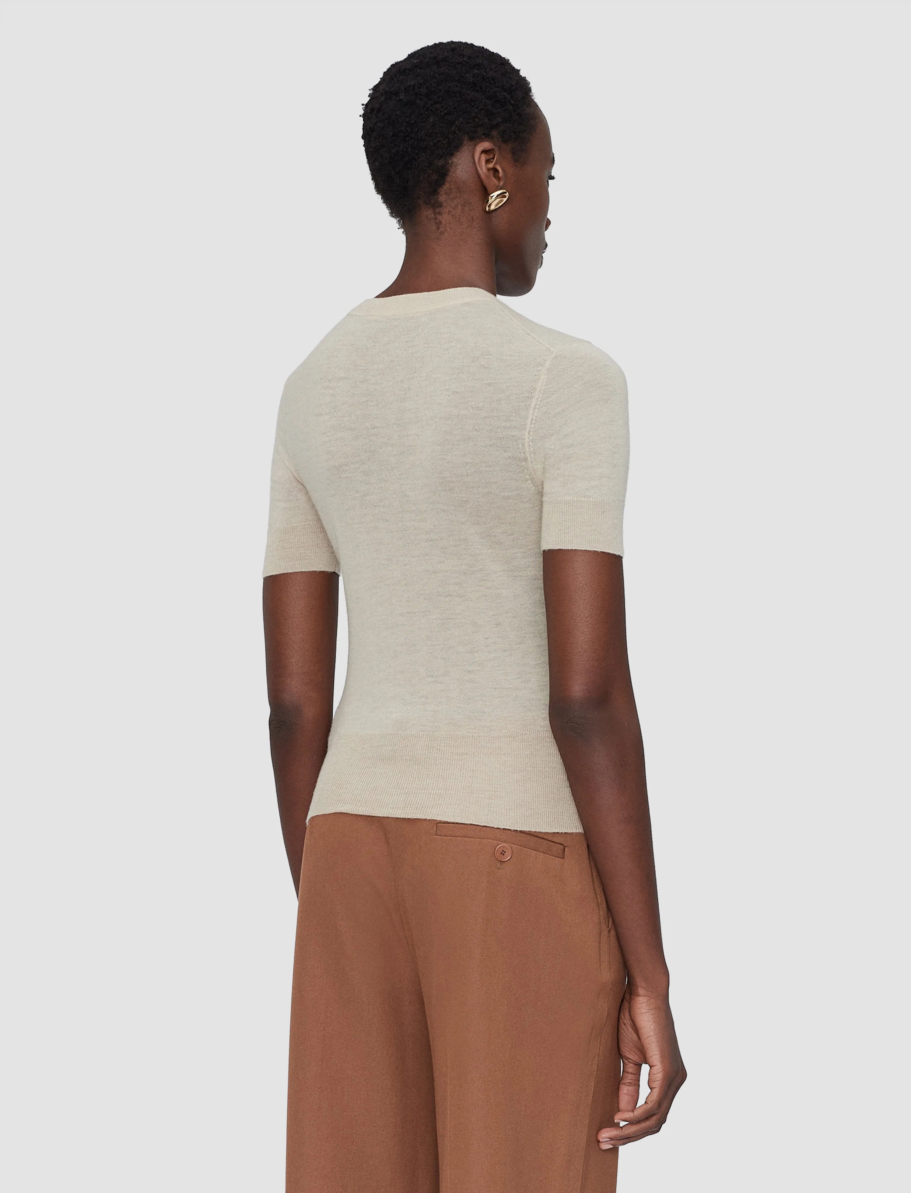 Person wearing a beige sweater and brown pants on a white background