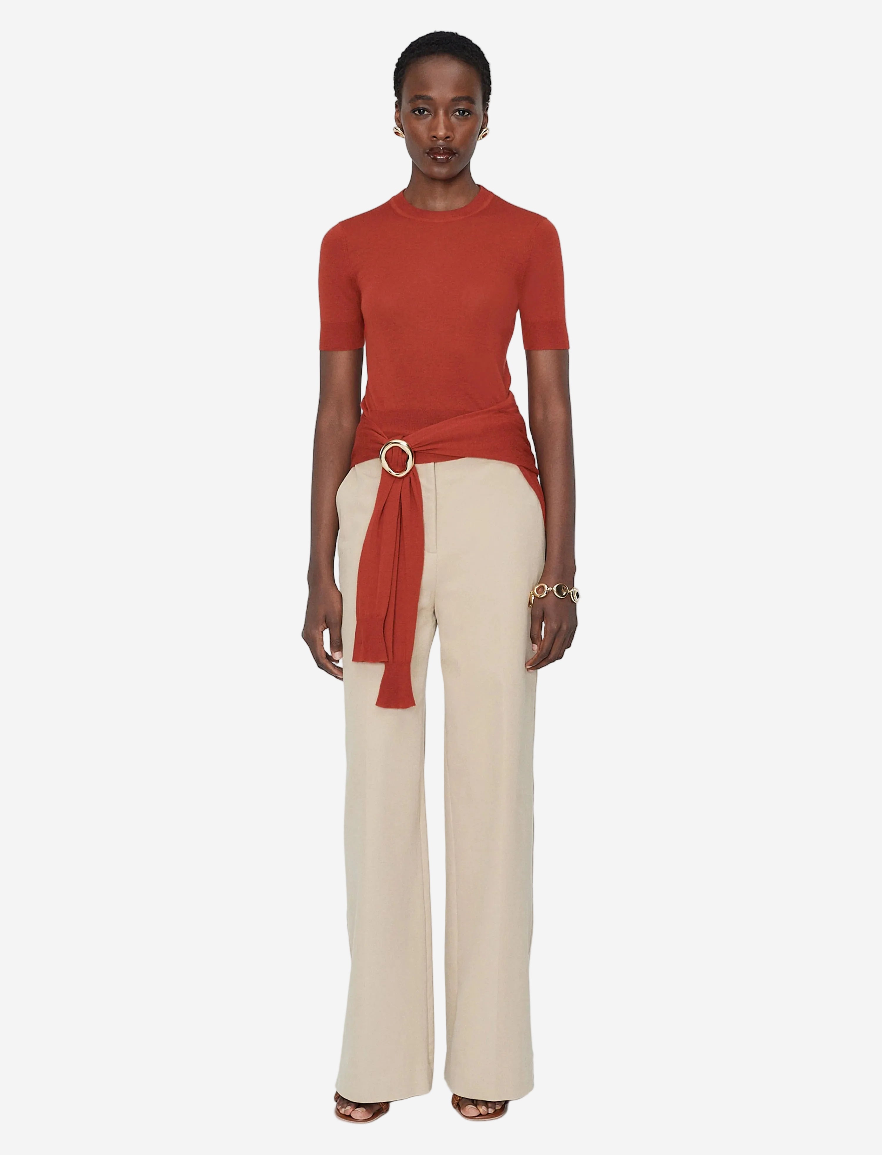 Woman wearing a red top and beige pants with a belt on a white background