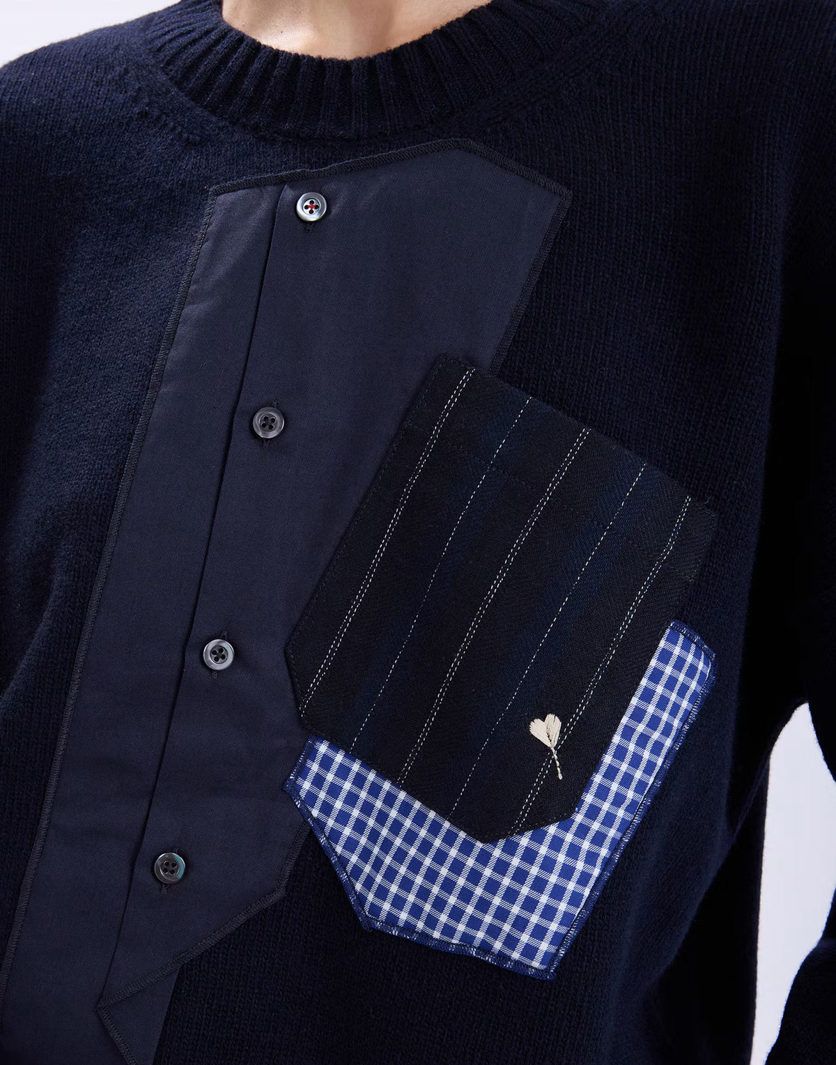 Close-up of the HIGH Casually sweater showing the shirt placket, pinstripe pocket, gingham trim and heart pin detail