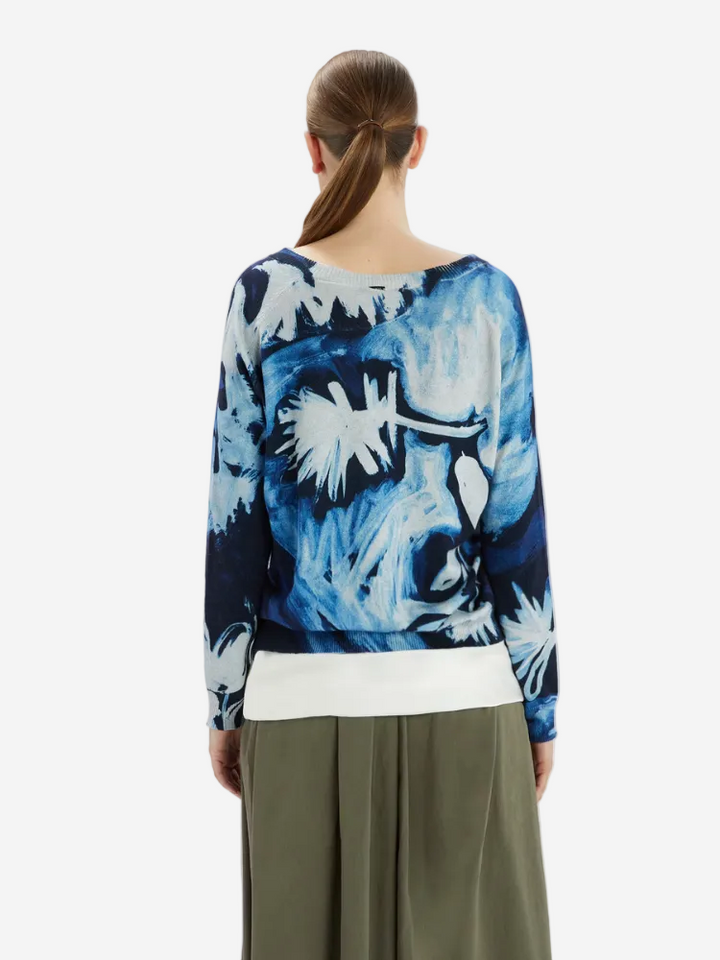 Person wearing a blue tie-dye top with a white band and green pants on a white background
