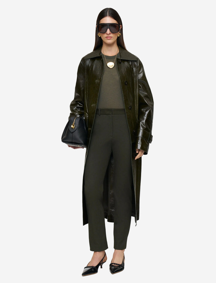 Woman wearing a long black coat, black pants, and sunglasses on a white background