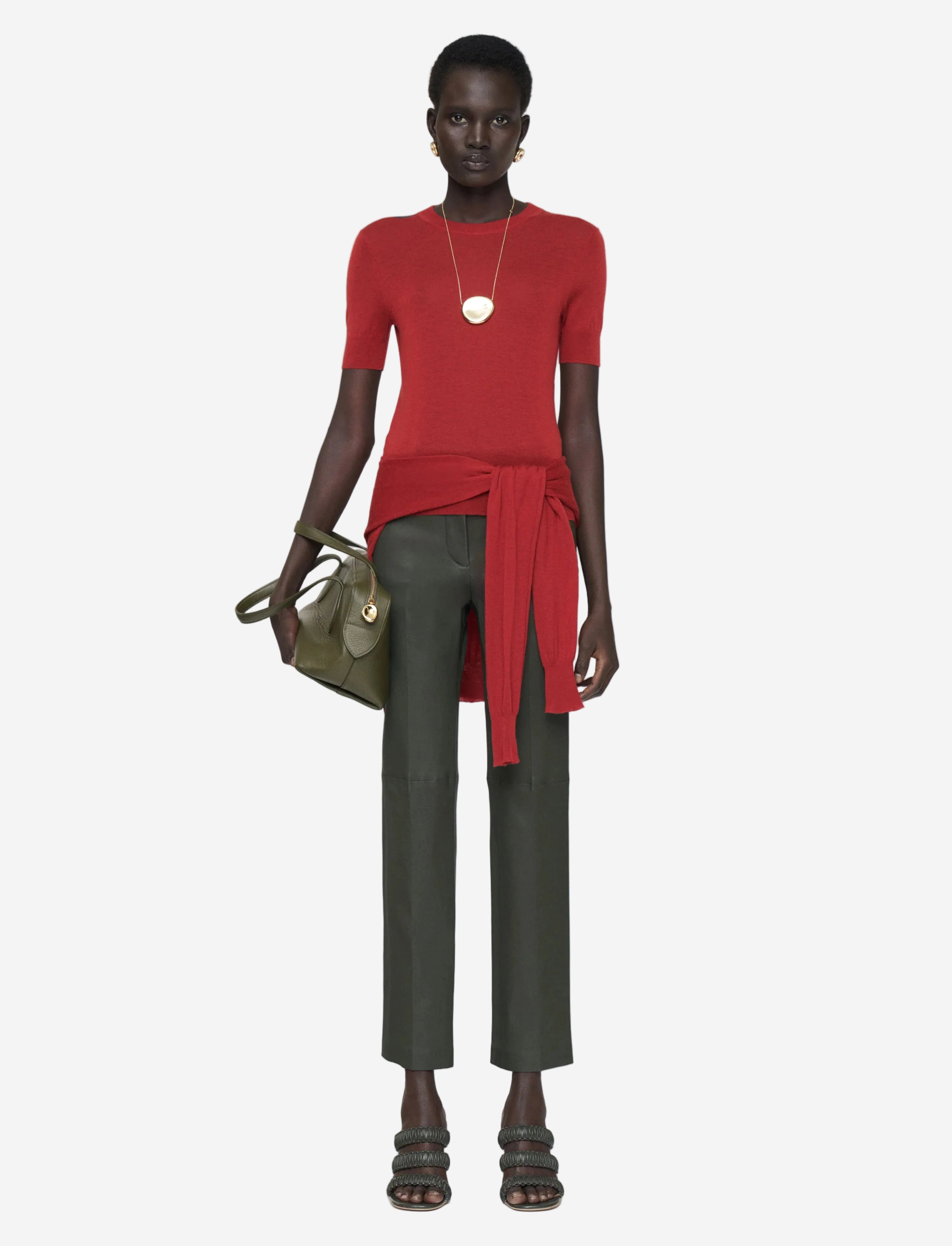 Woman wearing a red top and green pants with a handbag on a white background