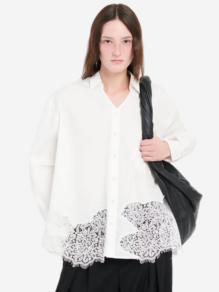 Woman wearing a white blouse with lace details on a plain background