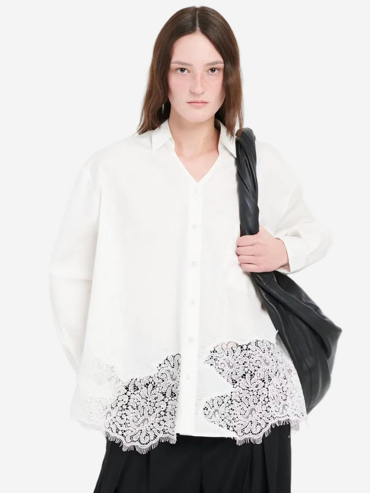Woman wearing a white blouse with lace details on a plain background
