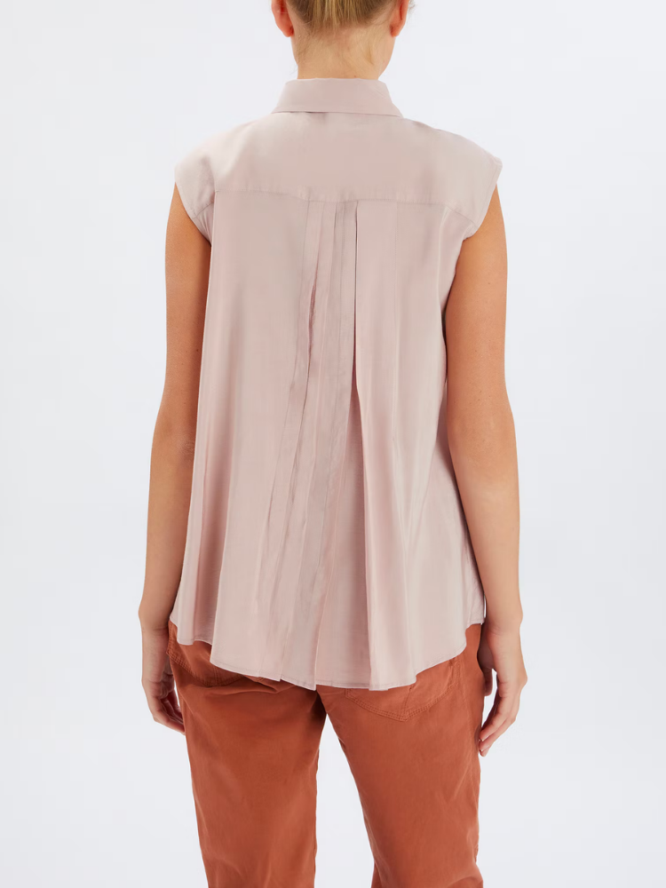 Person wearing a sleeveless beige top and brown pants on a white background