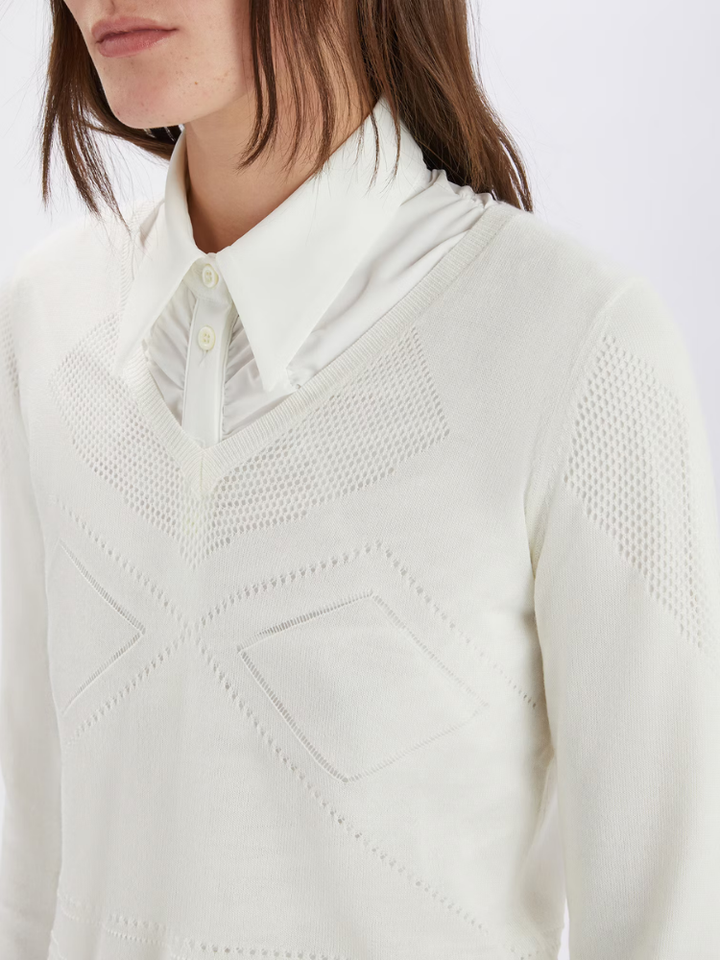Close-up of a person wearing a white textured sweater over a collared shirt.
