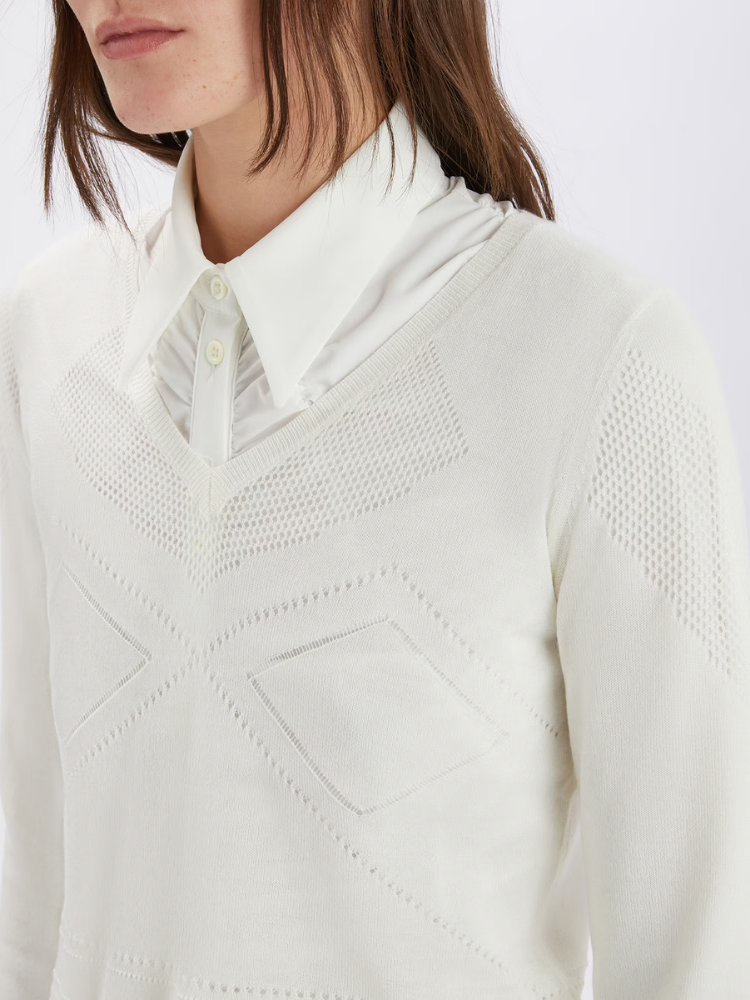 Close-up of a person wearing a white textured sweater over a collared shirt.