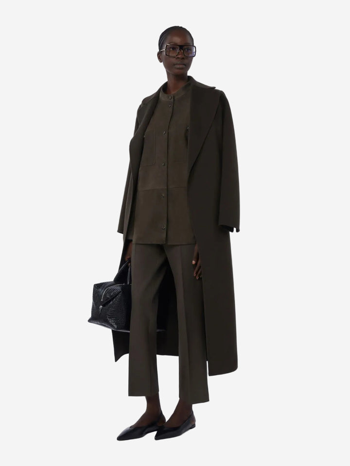 Person wearing a long dark green coat and pants on a white background