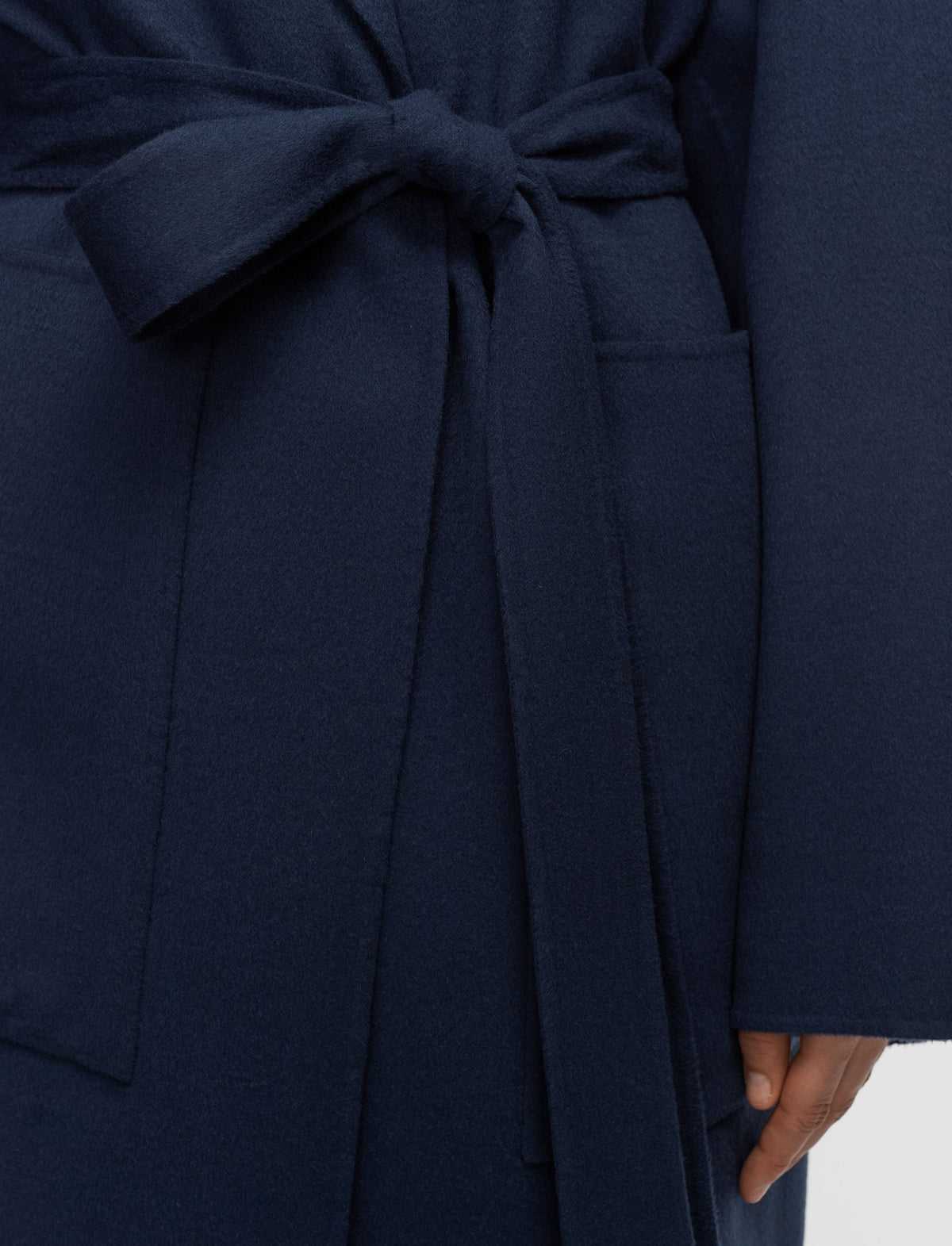 Close-up of a dark navy blue wrap coat with a matching tie belt and side pockets.