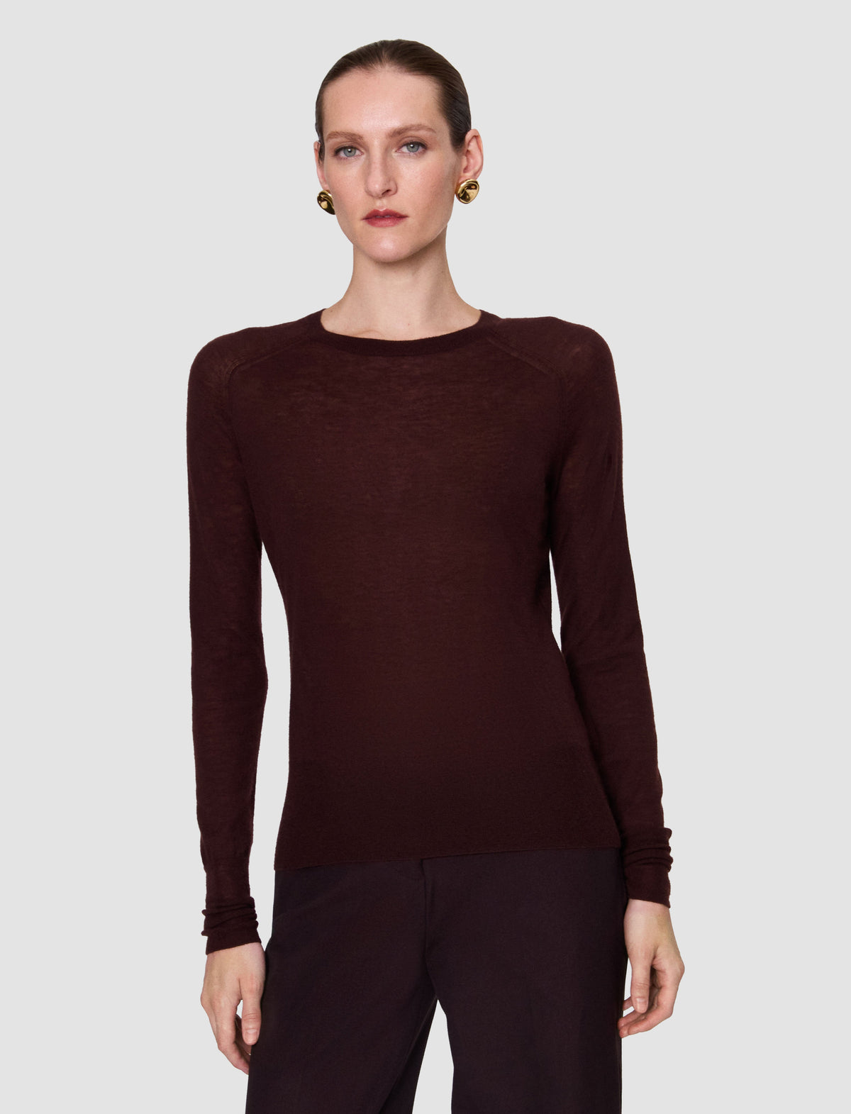 A model wearing a dark burgundy long-sleeve crewneck knit sweater from Christensen Copenhagen. 