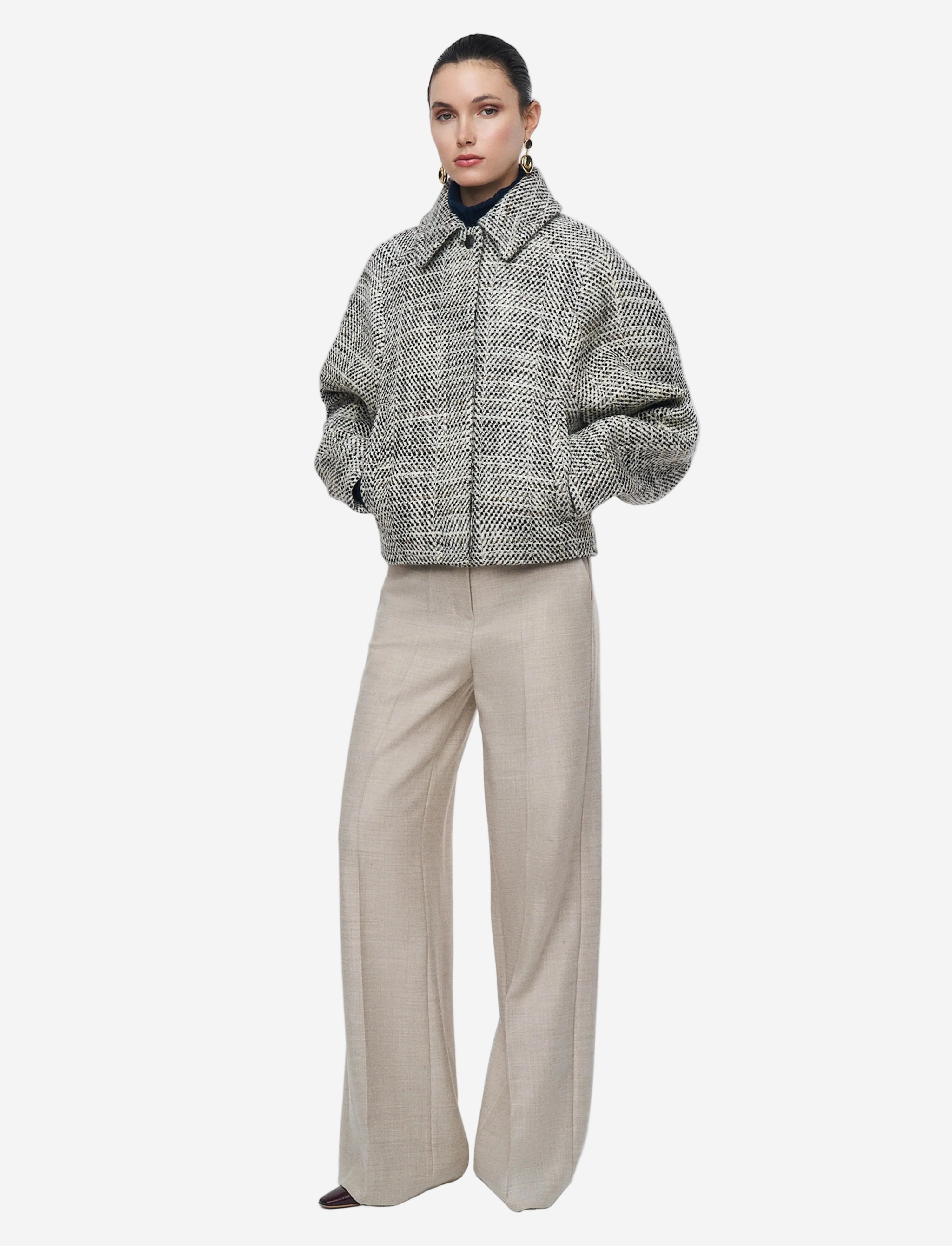 Person wearing a textured gray jacket and beige pants on a white background