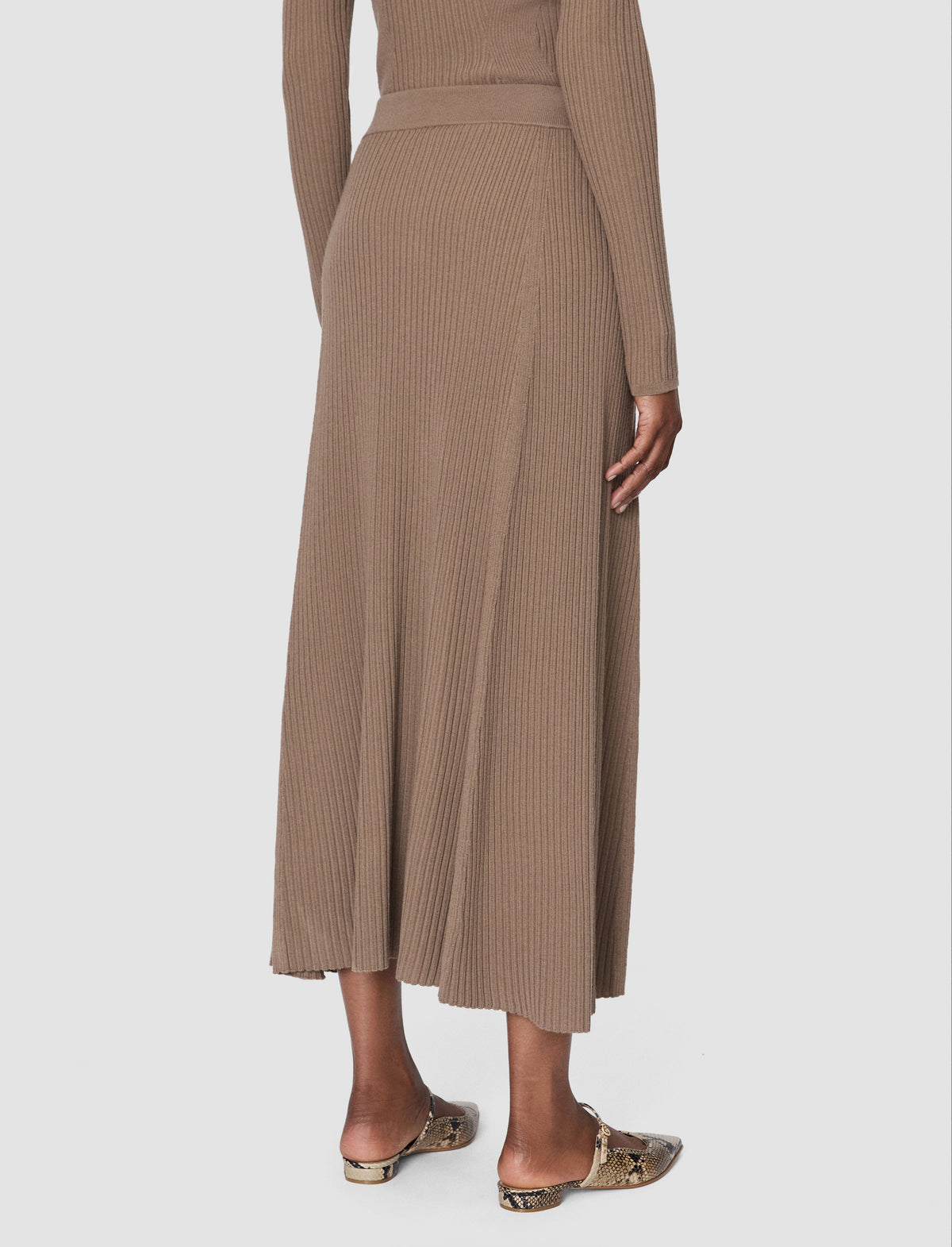 A model is shown from the back wearing a ribbed knit midi skirt in a warm taupe-brown colour from Christensen Copenhagen.  