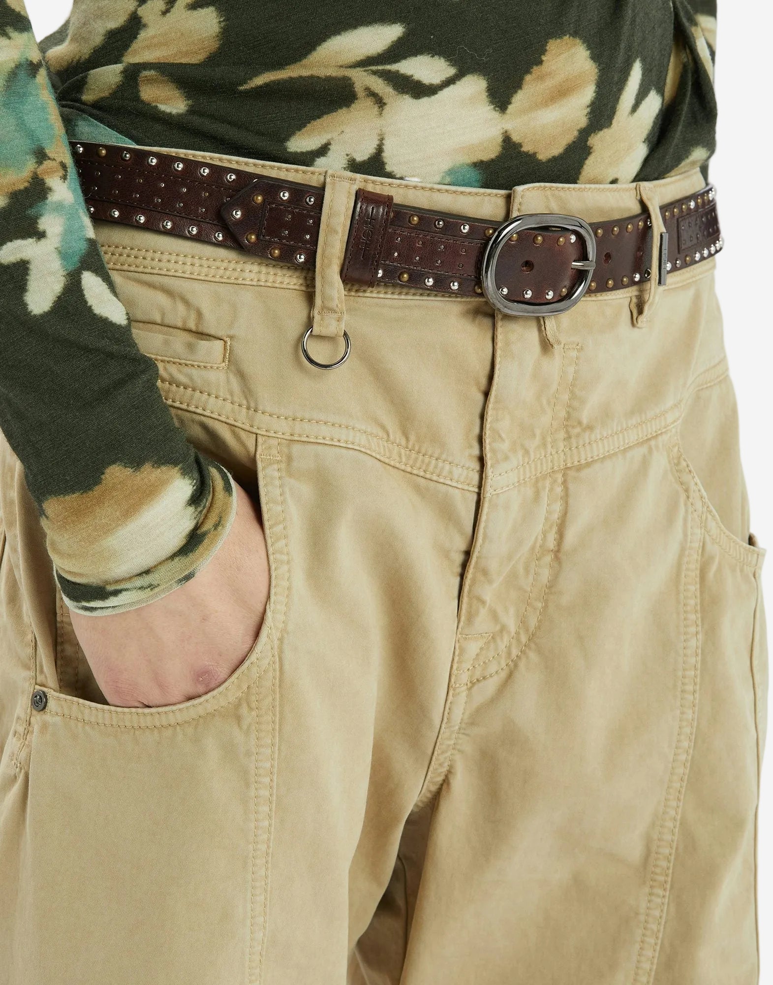 Close-up of beige pants with a brown belt and floral shirt sleeve.