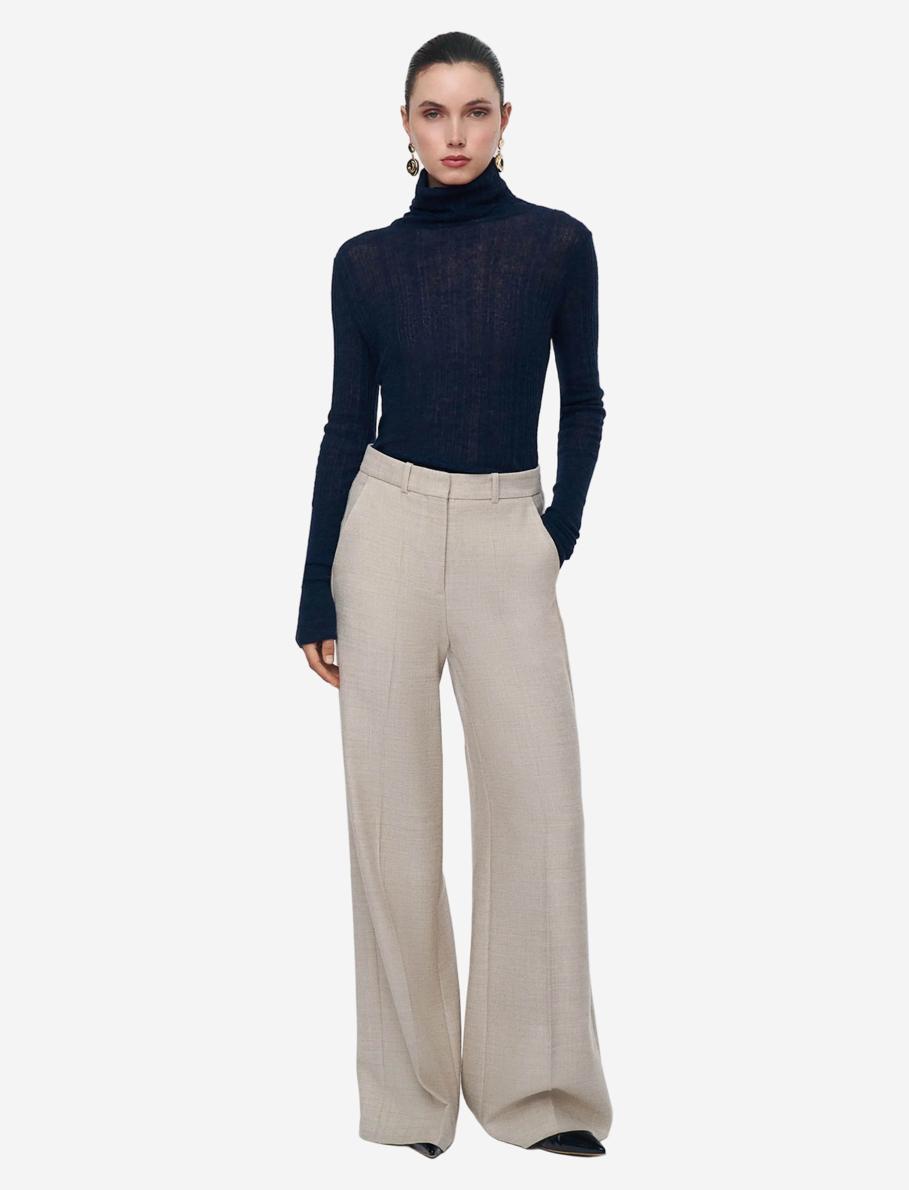 Person wearing a navy turtleneck and beige wide-leg pants on a white background