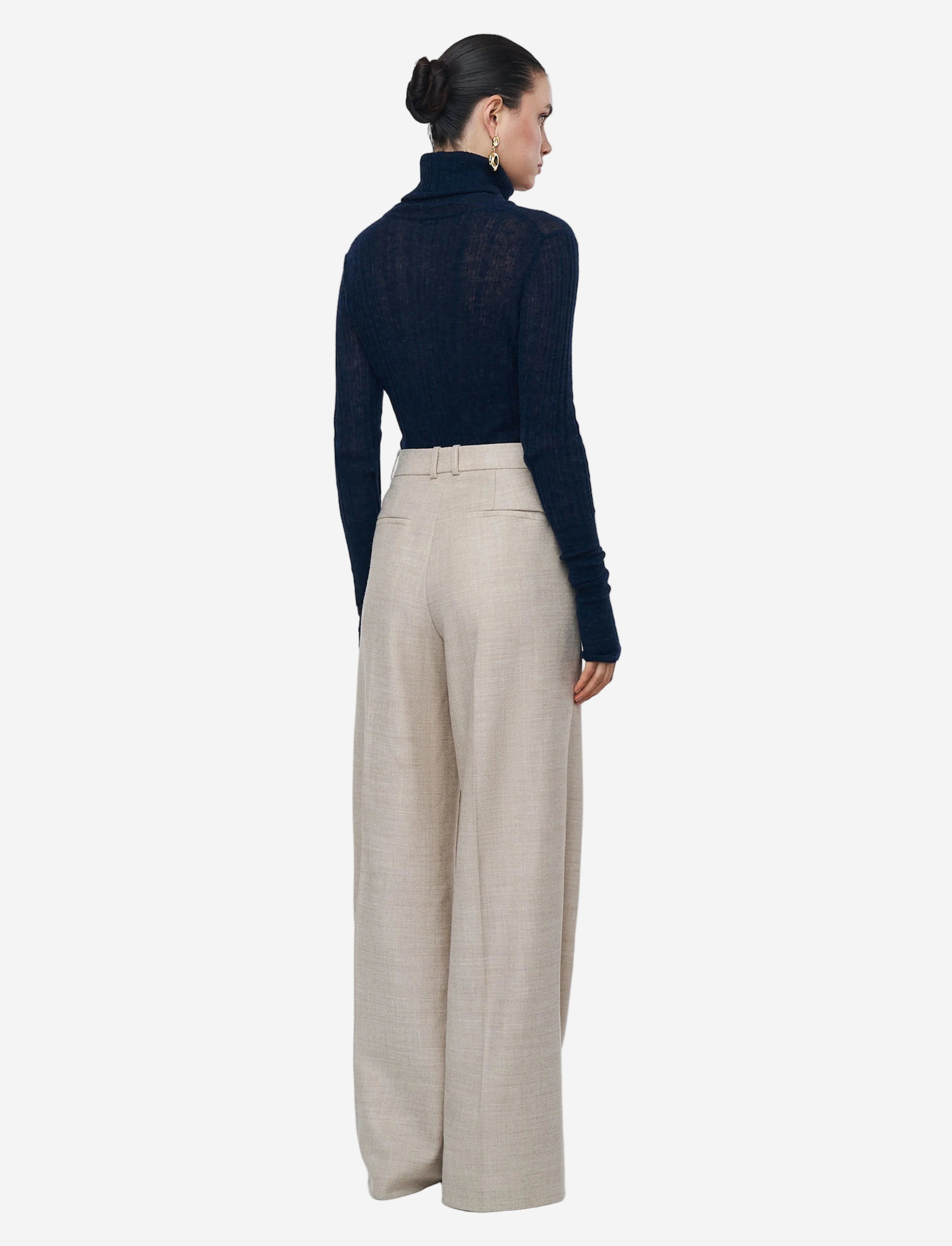 Woman wearing a navy turtleneck and beige wide-leg pants on a light gray background