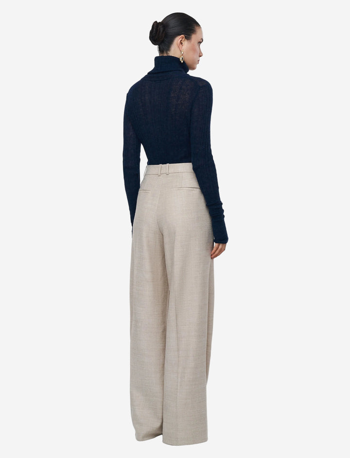 Woman wearing a navy turtleneck and beige wide-leg pants on a light gray background