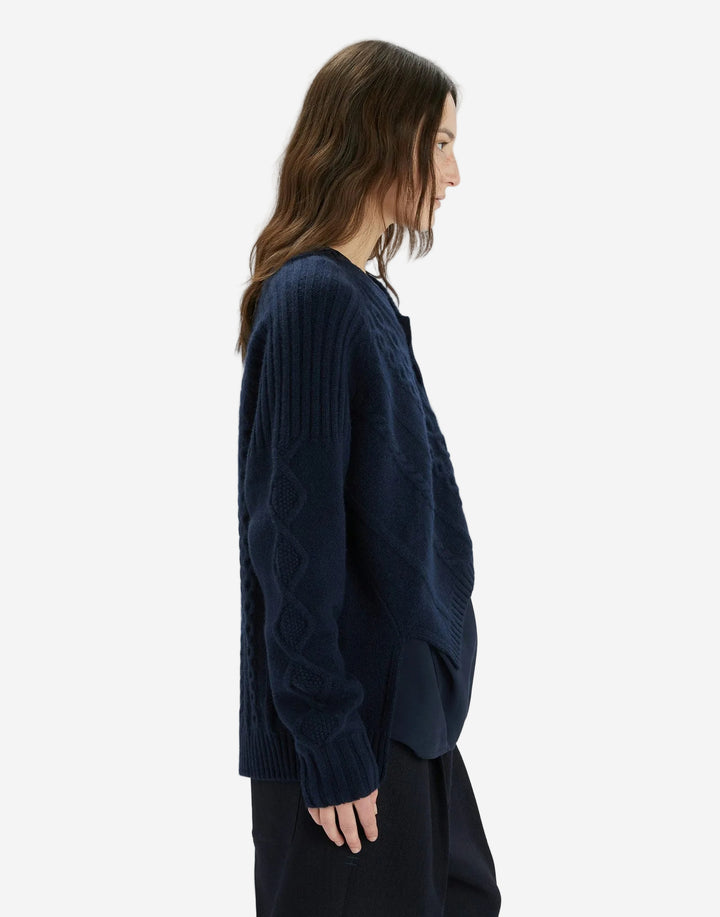 Person wearing a dark blue cardigan over a black top on a white background