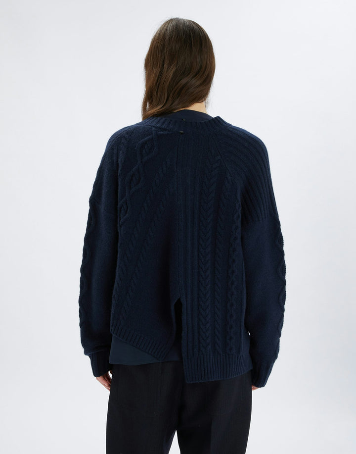 Person wearing a navy blue cable knit sweater on a white background