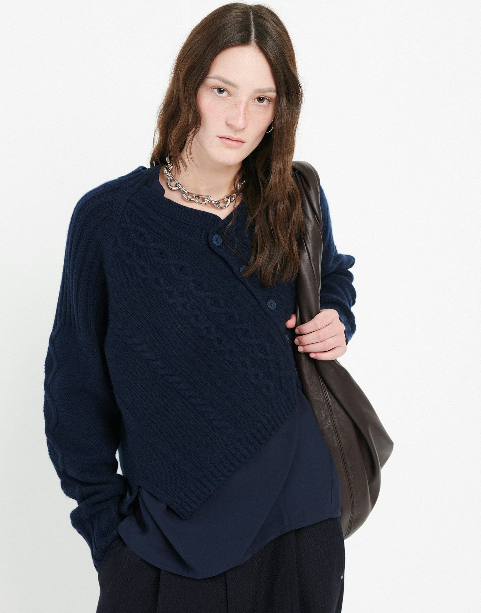 Woman wearing a navy blue cardigan holding a brown bag on a white background