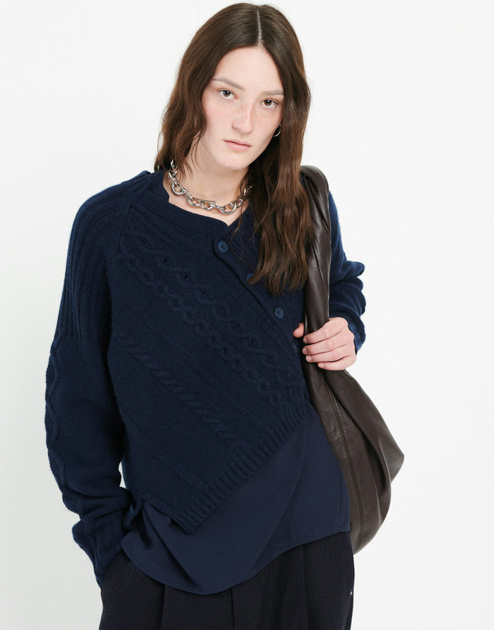Woman wearing a navy blue cardigan holding a brown bag on a white background