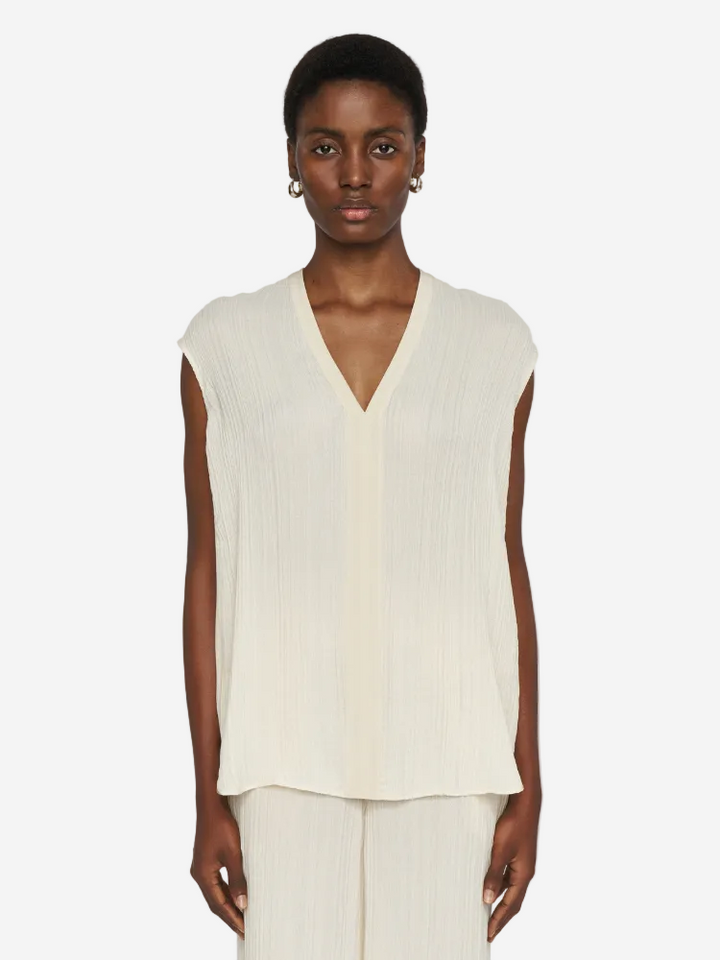 Person wearing a sleeveless cream top and pants on a white background