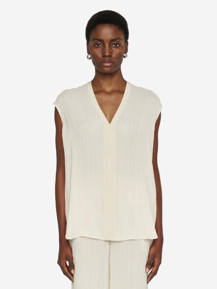 Person wearing a sleeveless cream top and pants on a white background