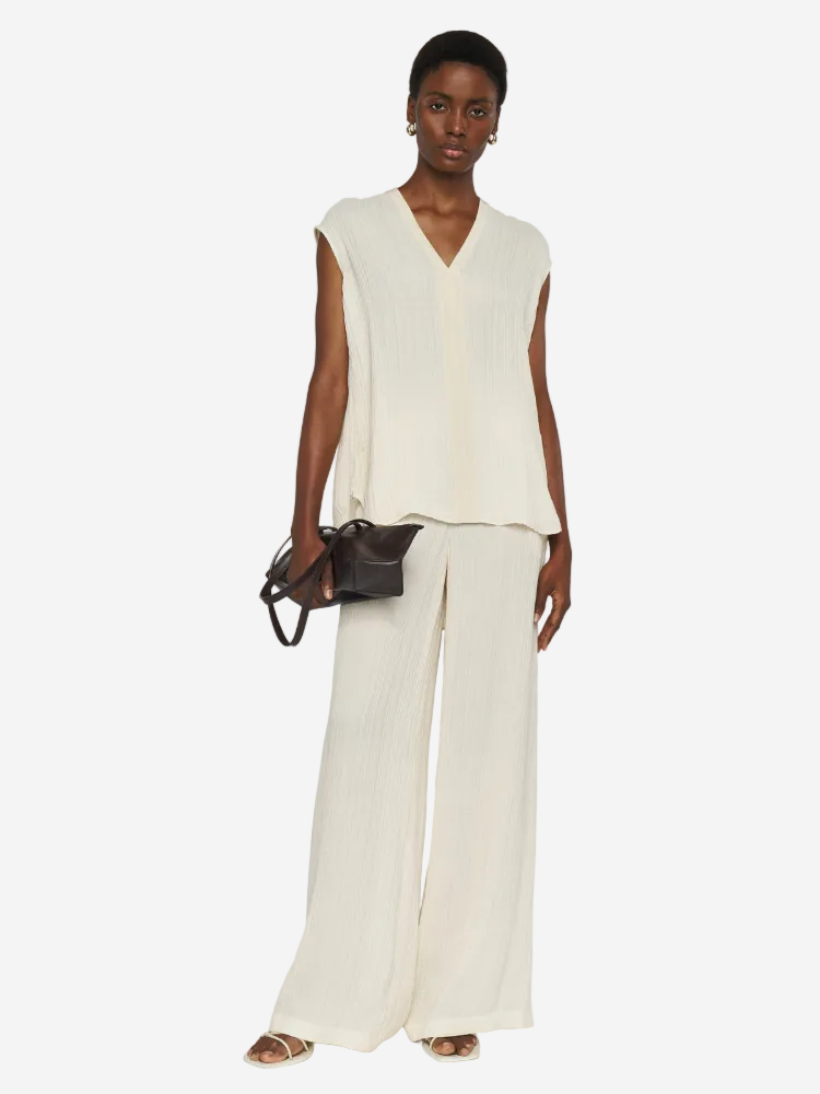 Woman wearing a sleeveless cream top and wide-leg pants against a white background
