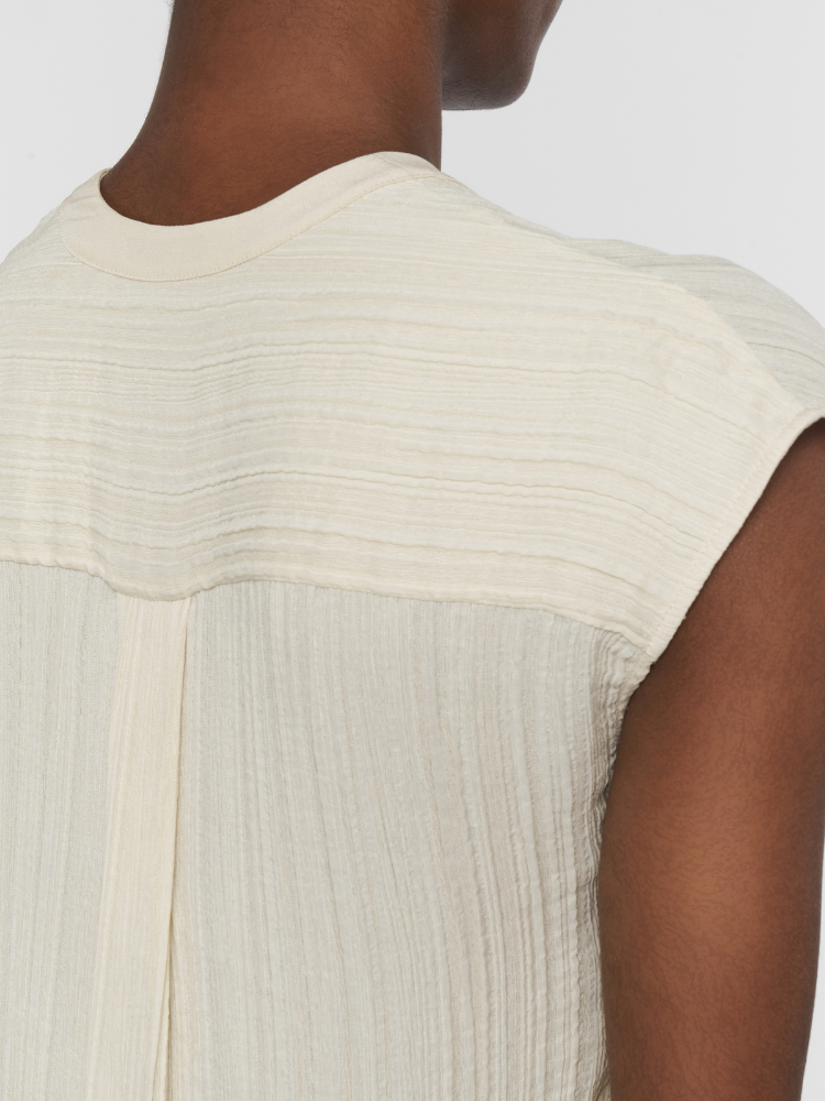 Close-up of a beige sleeveless top worn by a person on a plain background
