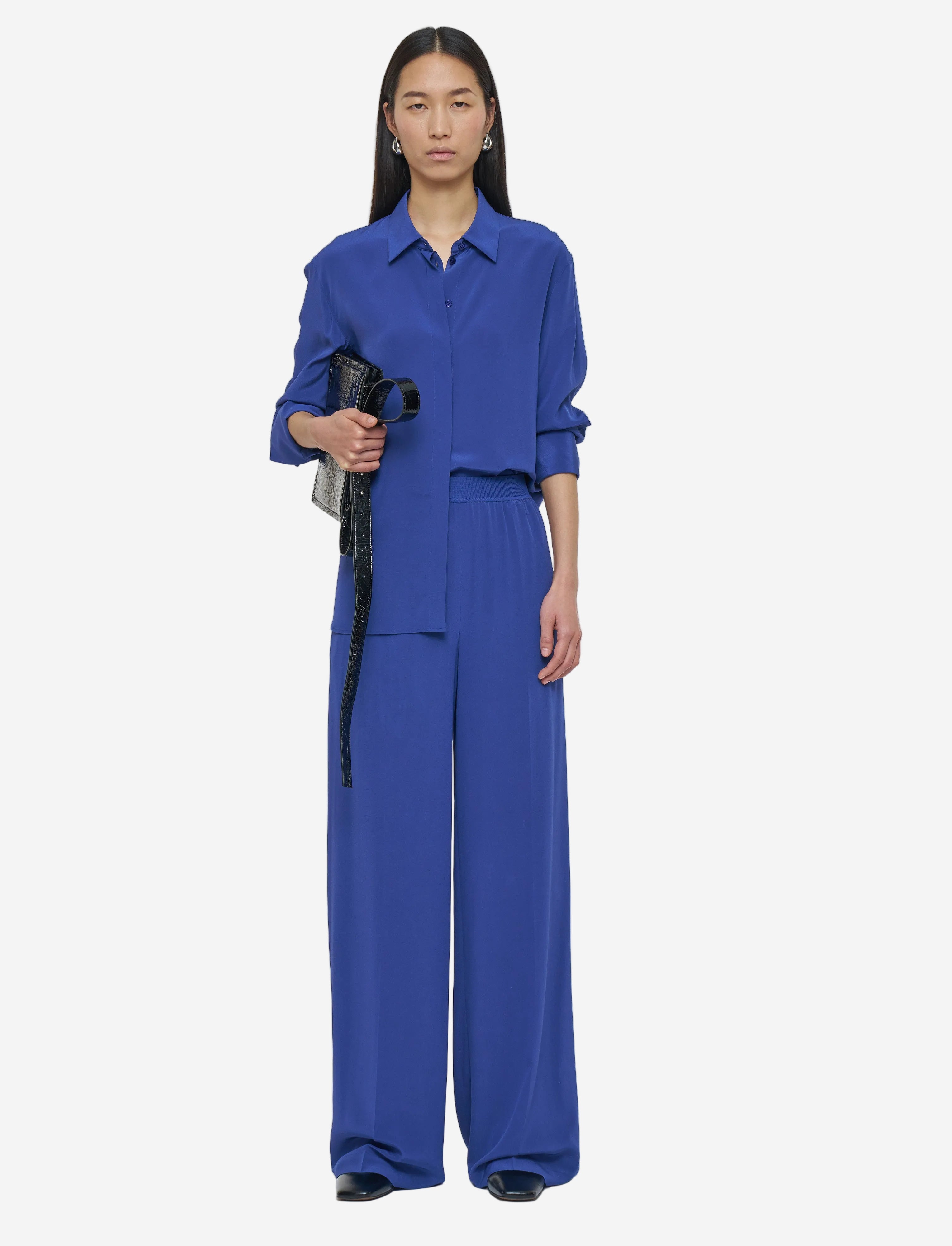 Person wearing a blue outfit holding a black bag on a white background