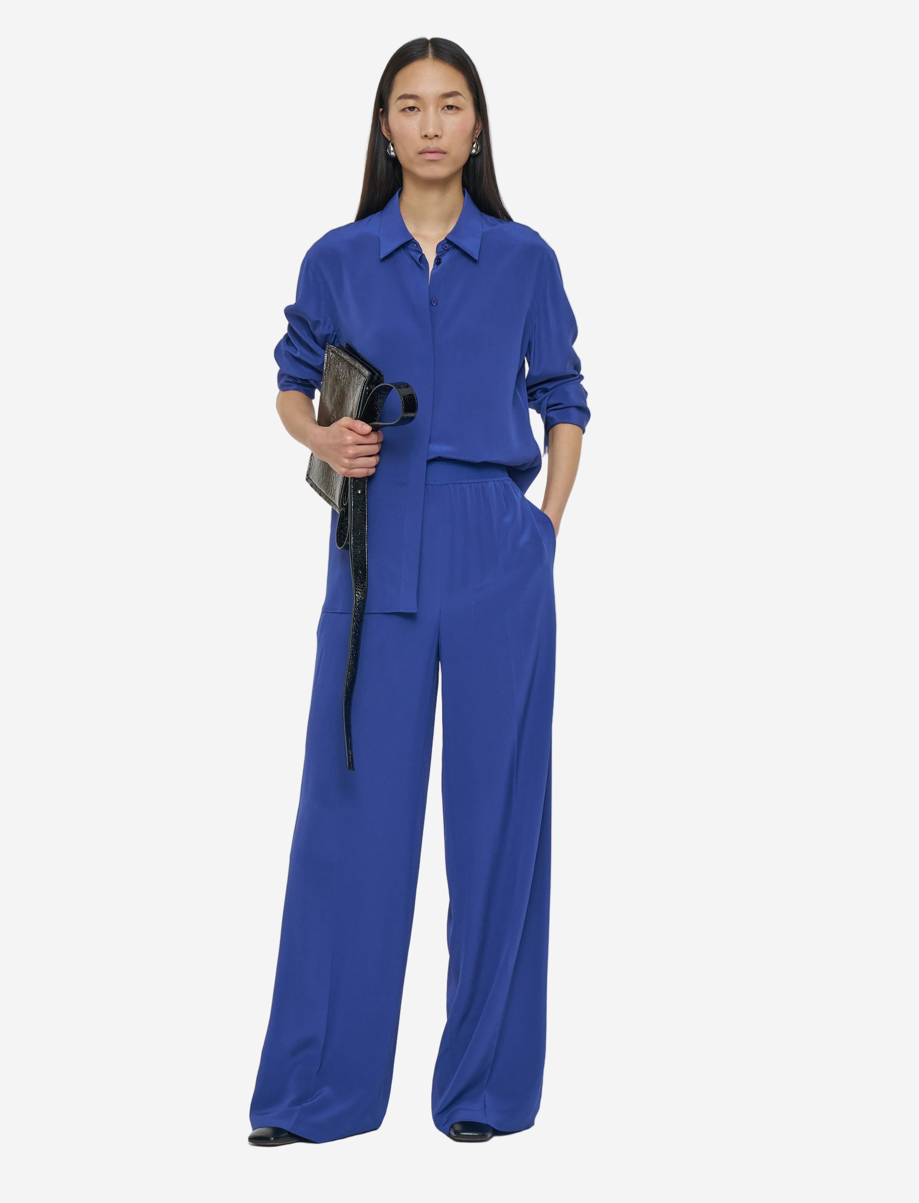 Person wearing a blue outfit holding a black bag on a white background