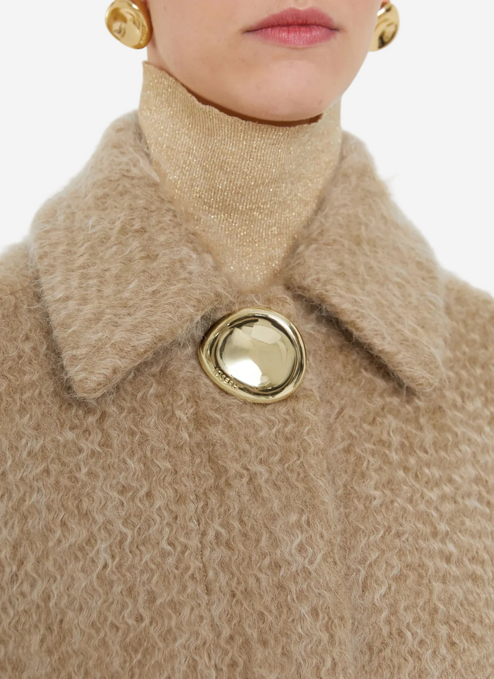 Close-up of a beige textured coat with a gold button and matching earrings on a white background