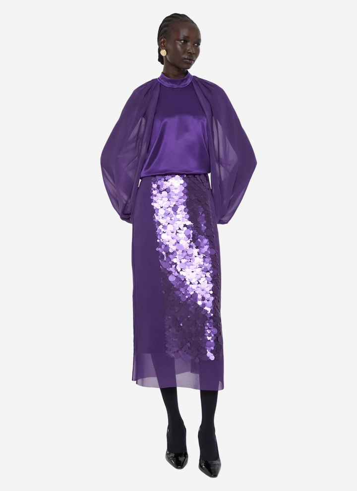 Person wearing a purple outfit with a sequin skirt on a white background