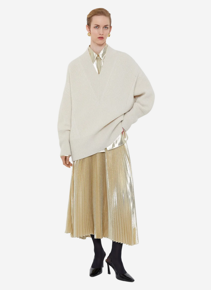 Person wearing a cream sweater and beige pleated skirt on a white background