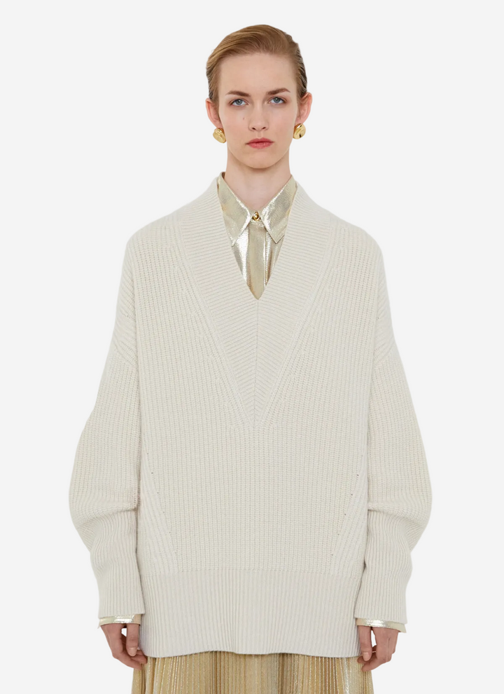 Person wearing a cream-colored sweater over a light shirt with a plain background
