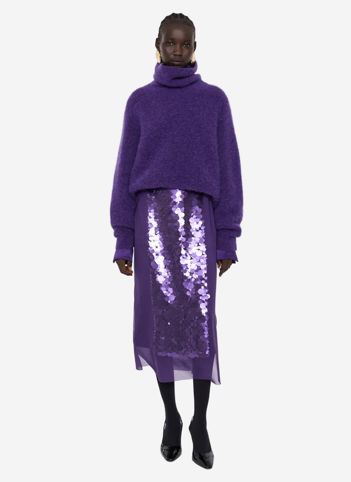 Person wearing a purple sweater and sequin skirt on a white background