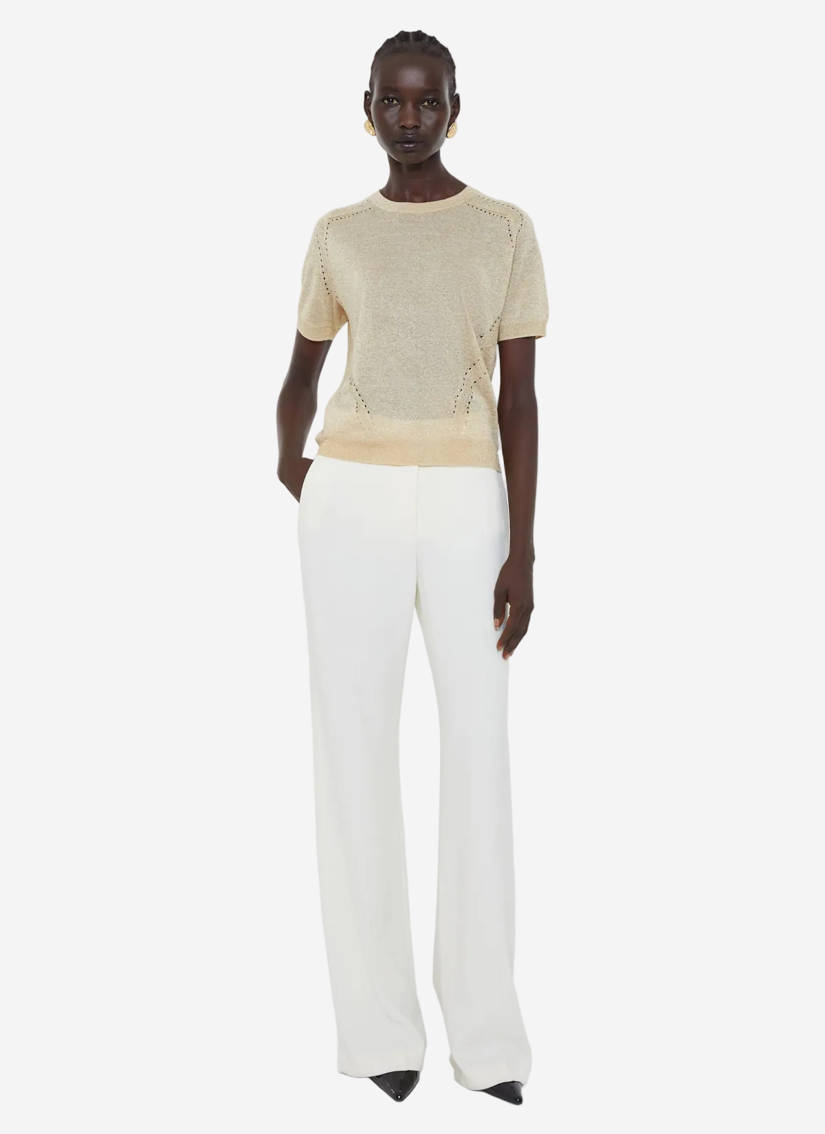 Woman wearing a beige knit top and white pants on a light gray background