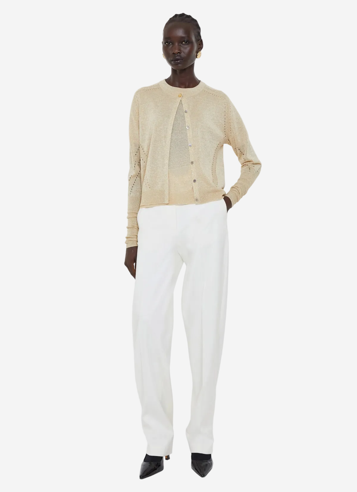 Person wearing a beige cardigan and white pants on a white background