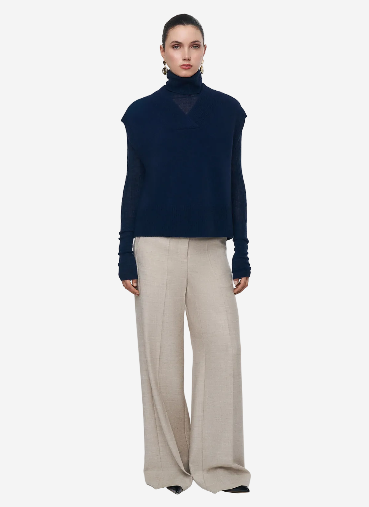 Woman wearing a navy blue turtleneck sweater and beige pants on a white background