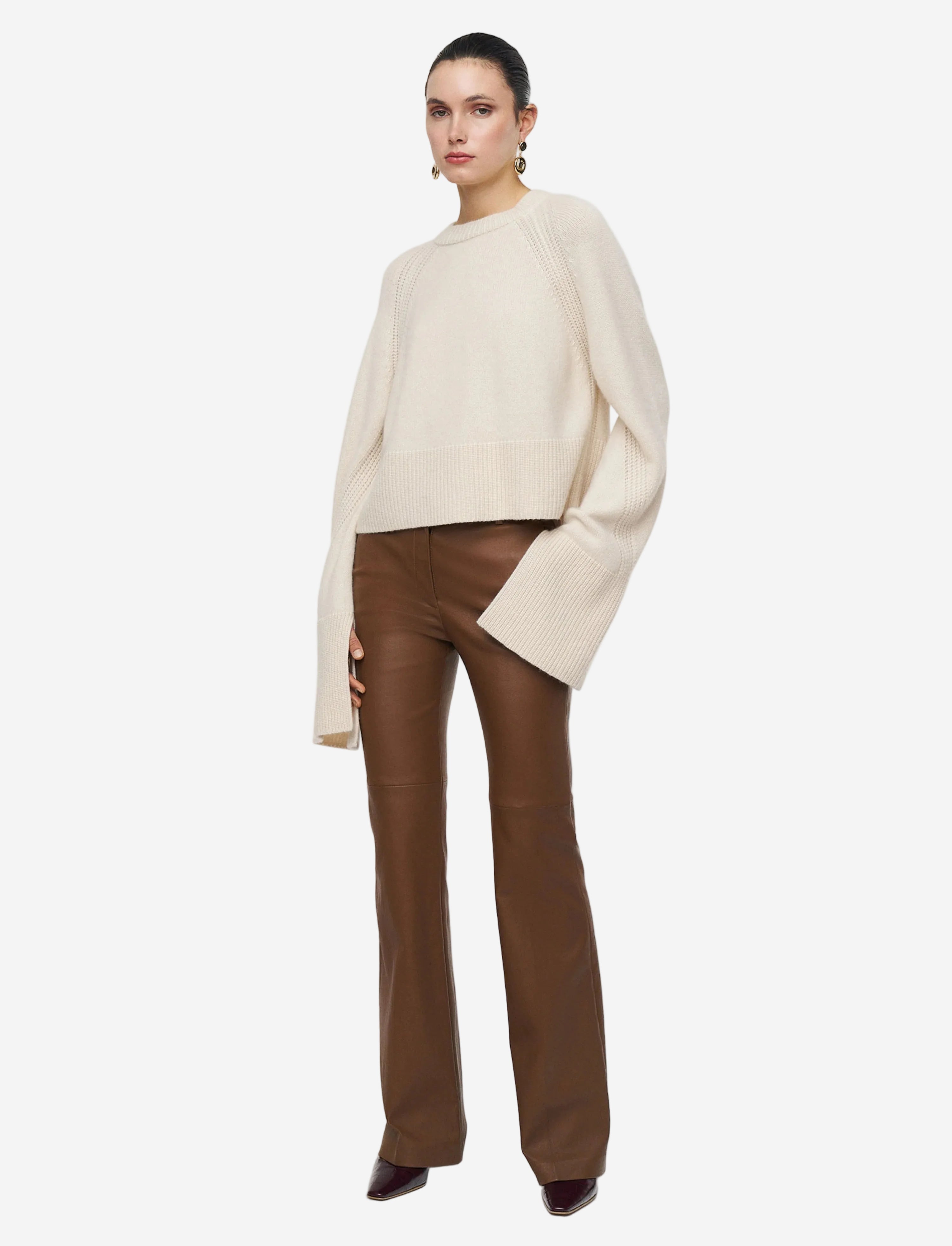 Woman wearing a cream sweater and brown pants on a white background