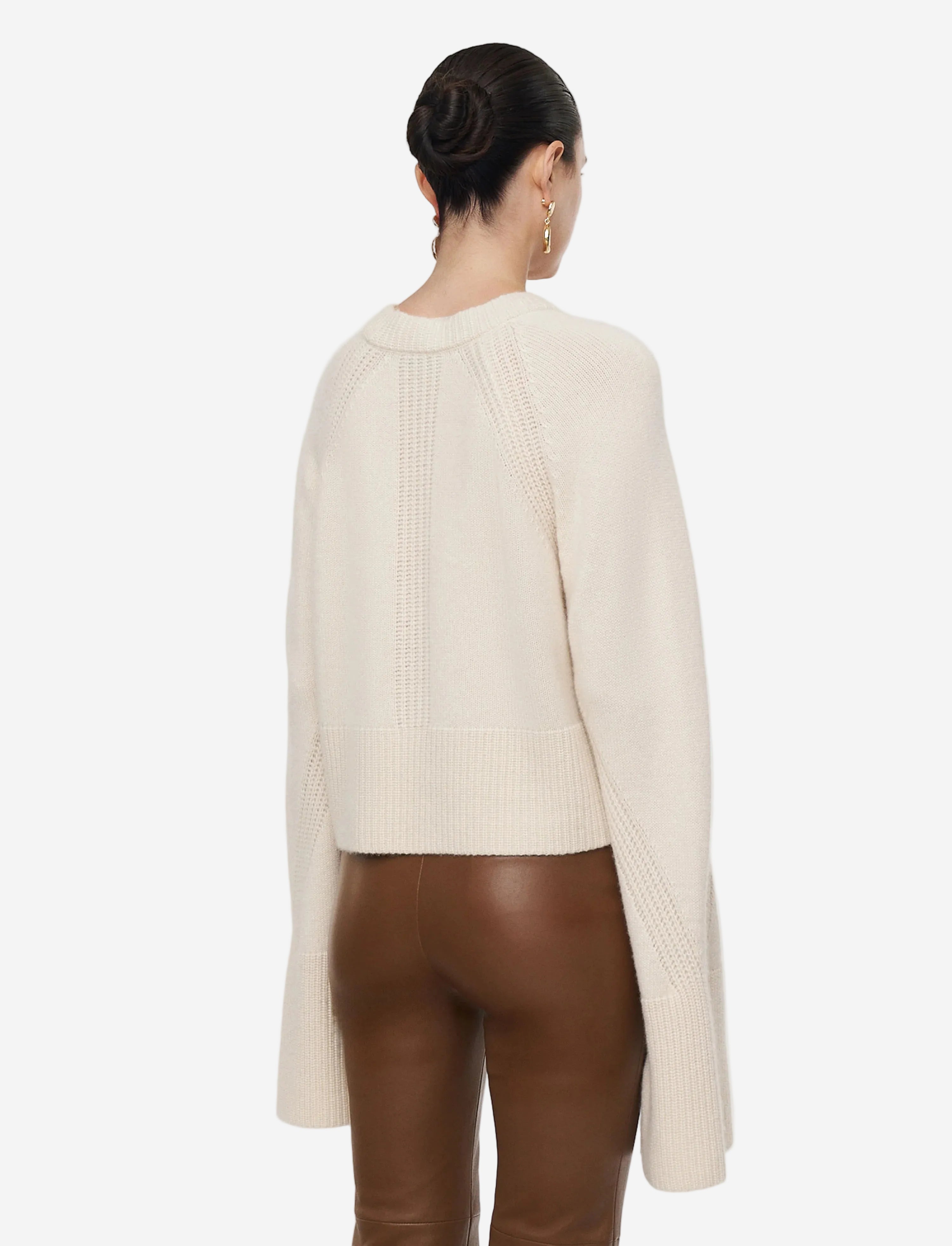 Person wearing a cream sweater and brown pants on a light gray background