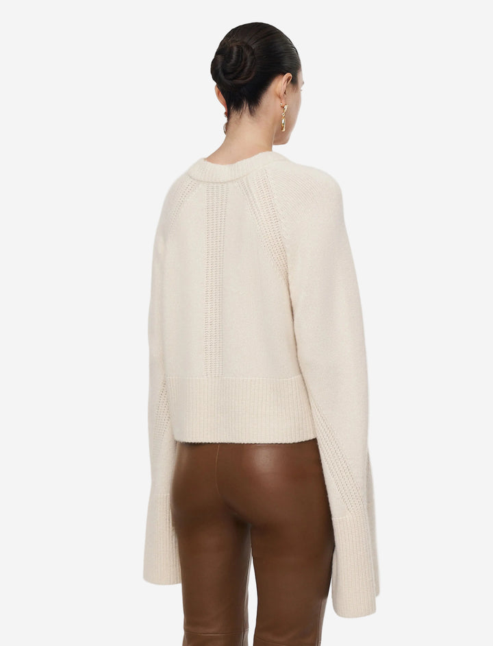 Person wearing a cream sweater and brown pants on a light gray background