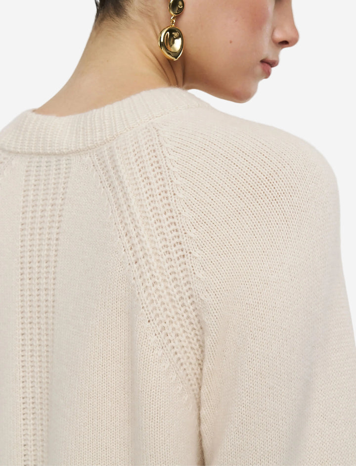 Close-up of a person wearing a beige knit sweater with a plain background