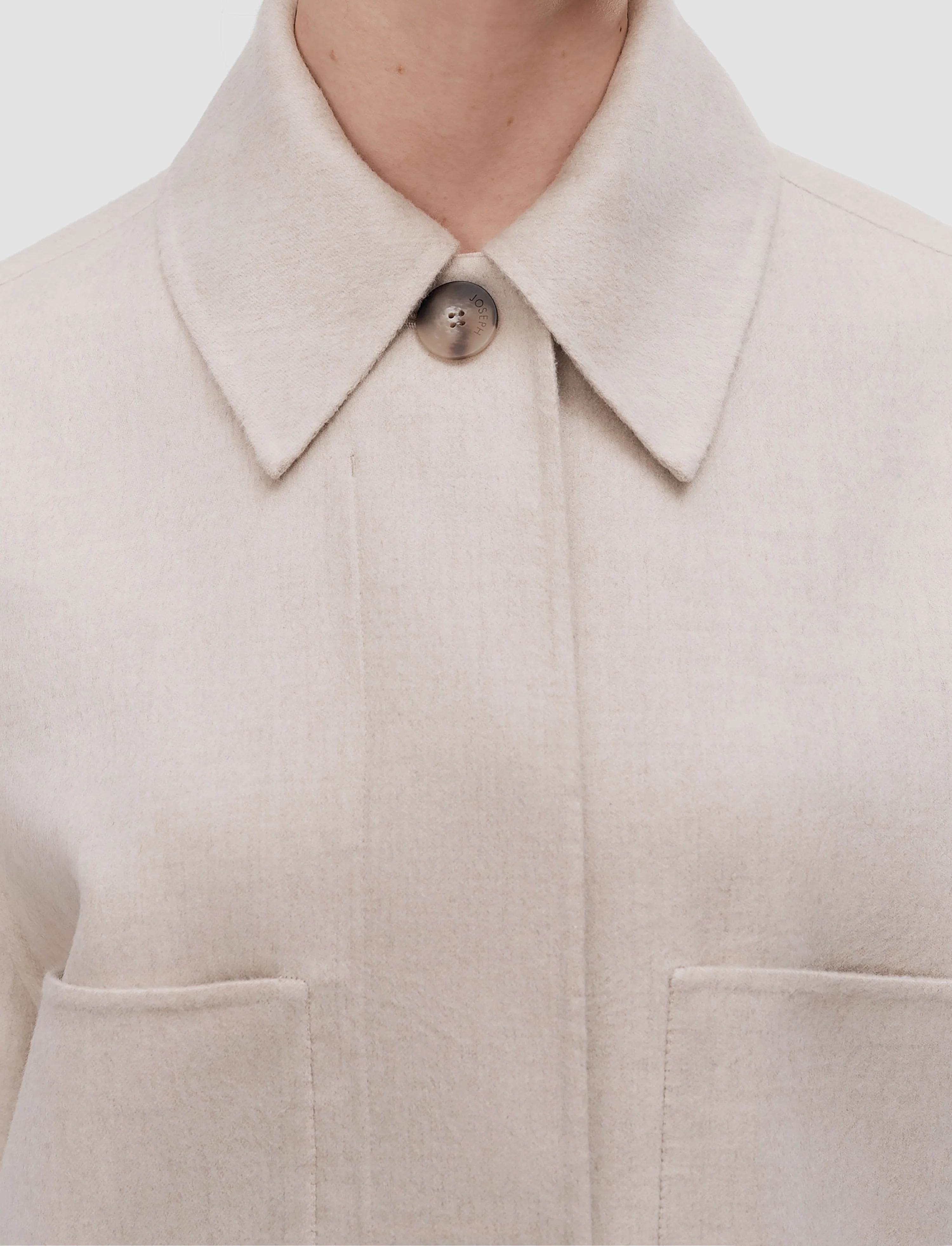 Close-up of a beige coat with a collar and button on a light background