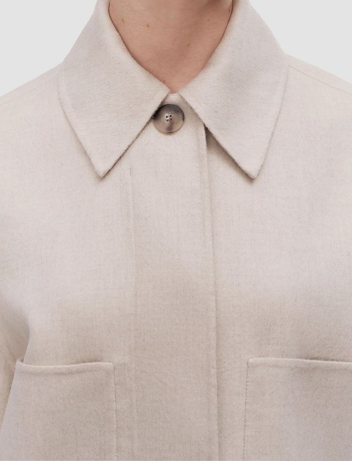 Close-up of a beige coat with a collar and button on a light background