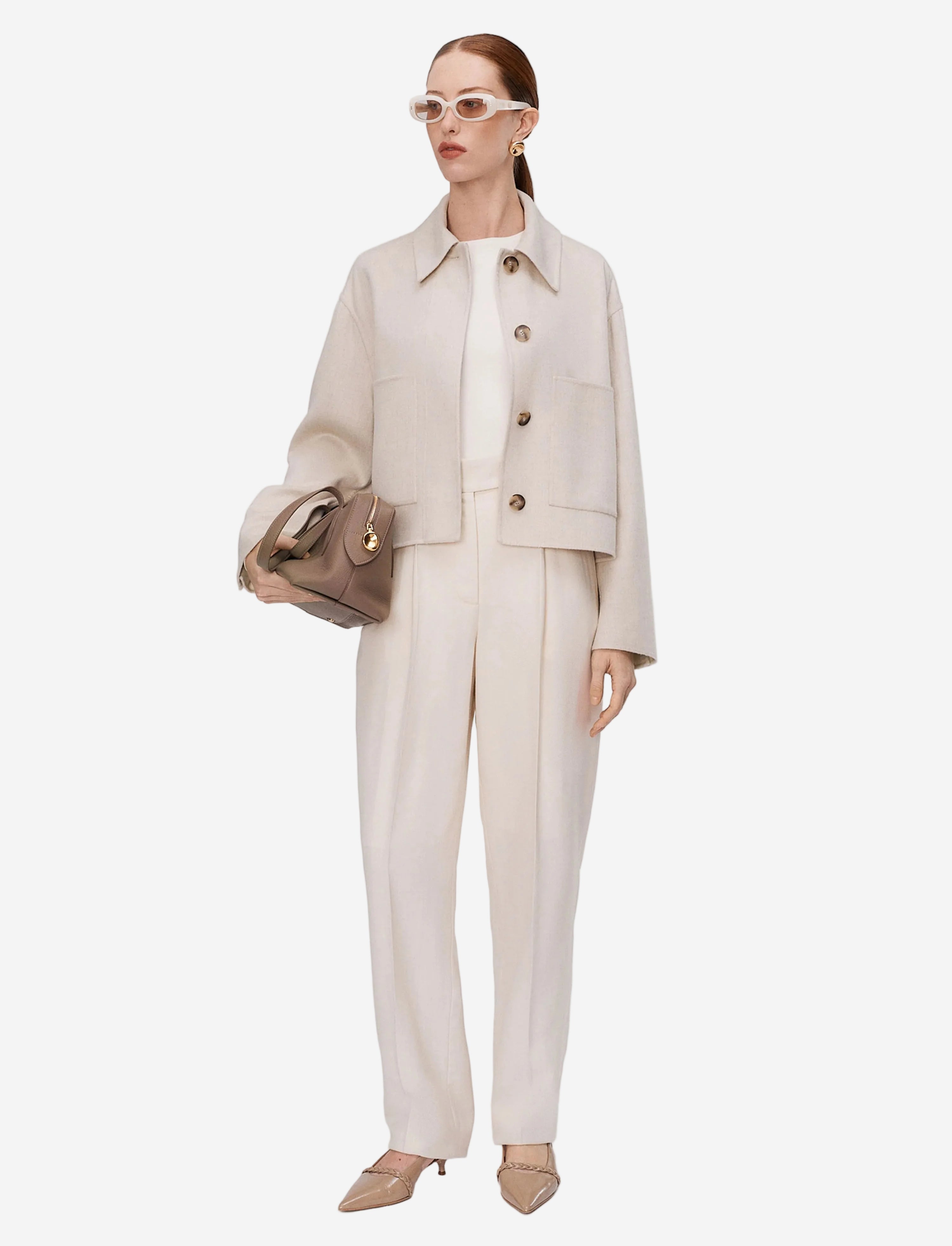 Woman wearing a beige suit with sunglasses and a handbag on a white background