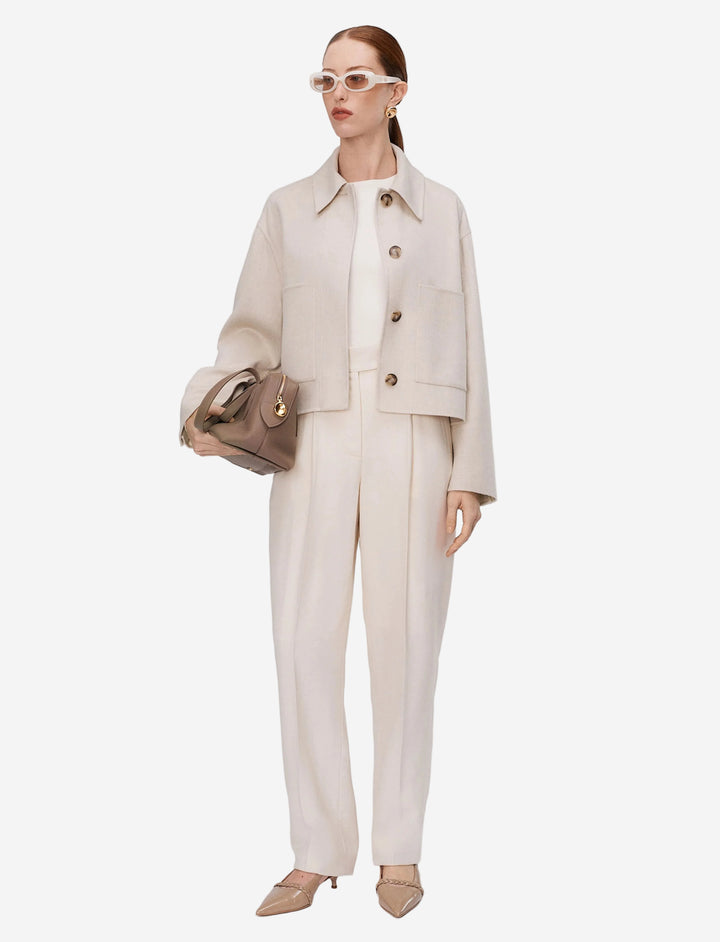 Woman wearing a beige suit with sunglasses and a handbag on a white background