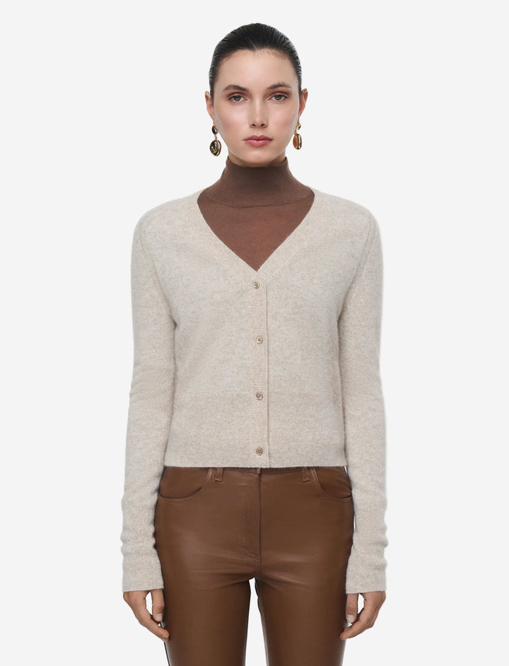 Woman wearing a beige cardigan over a brown turtleneck and brown pants on a white background