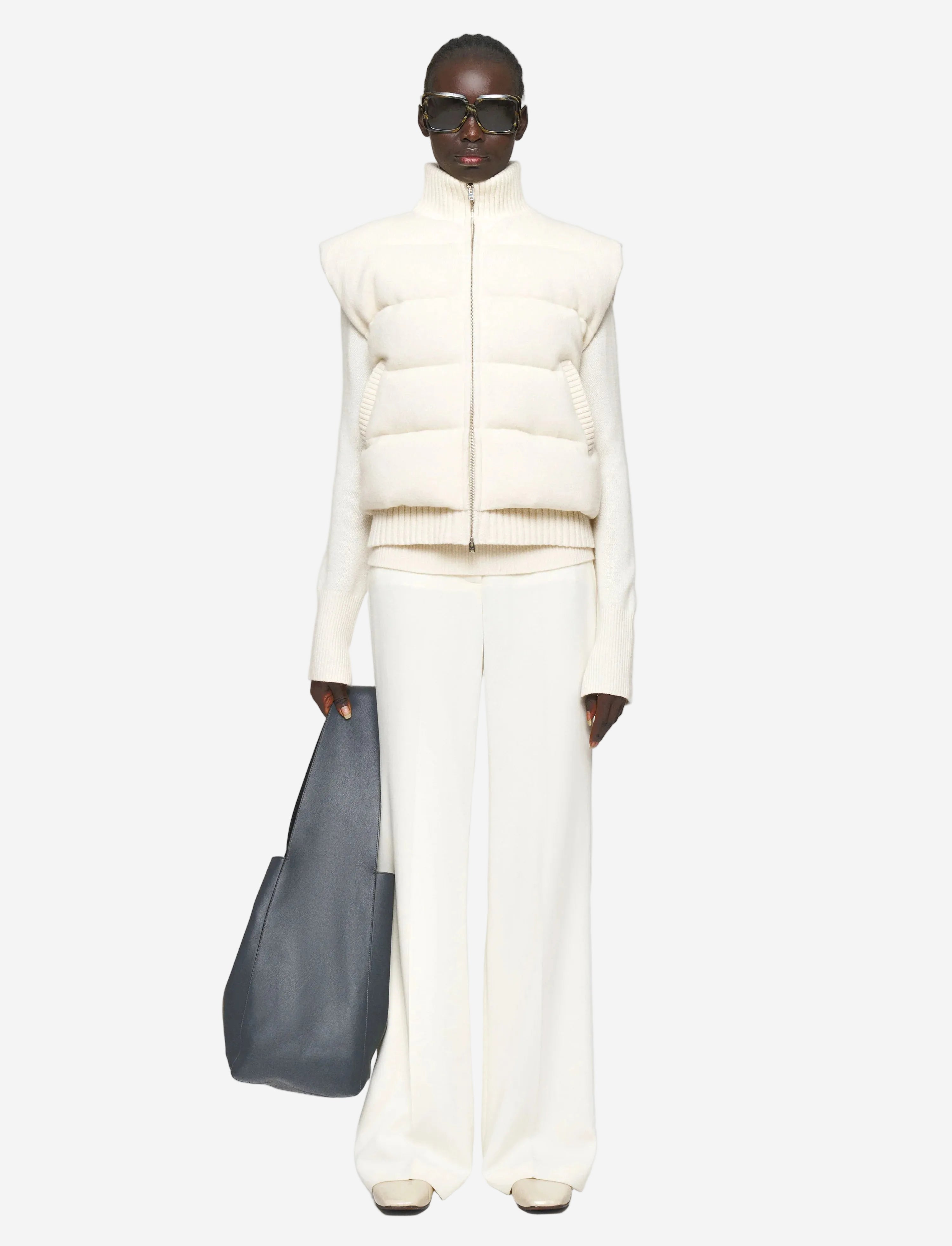 Person wearing a white puffer vest and pants with a gray bag on a light gray background