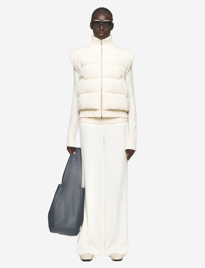 Person wearing a white puffer vest and pants with a gray bag on a light gray background