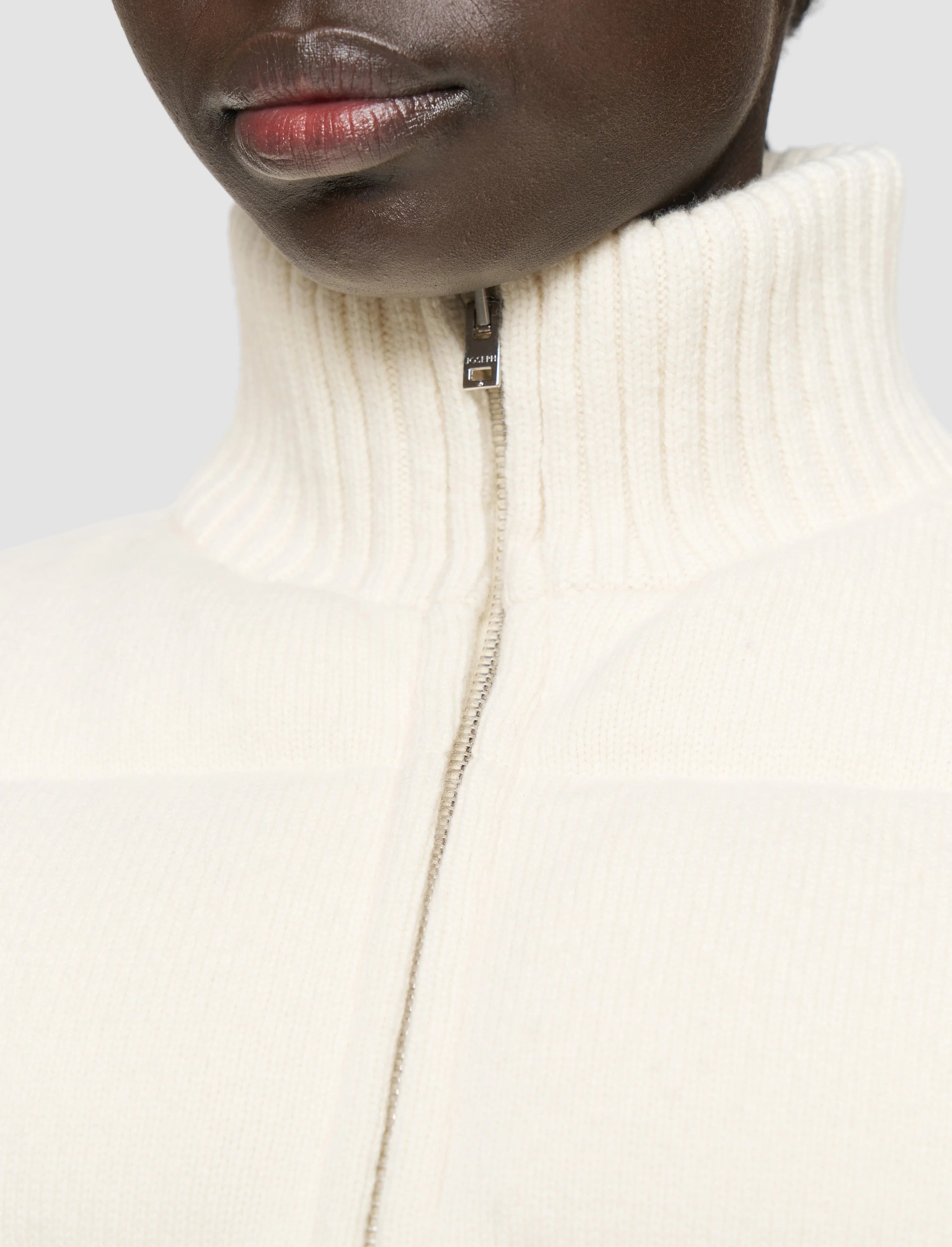 Close-up of a person wearing a cream-colored turtleneck sweater with a zipper.